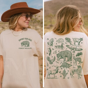 May include: Beige t-shirt with a green graphic of a bear and the text "SUPPORT YOUR LOCAL FOREST WILDLIFE." The back of the shirt features various green illustrations of forest animals. The person is wearing a brown hat and sunglasses.
