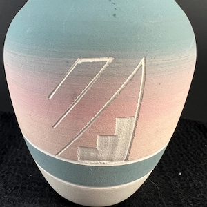 May include: A ceramic vase with a light blue, pink, and white ombre design. The vase has a geometric pattern carved into the surface.