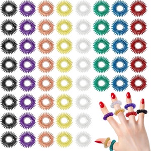 Puede incluir: Un conjunto de 50 anillos de acupresión de colores, con una mano que lleva varios anillos en diferentes dedos. Los anillos son de metal y tienen una textura puntiaguda. Los anillos están disponibles en negro, morado, naranja, amarillo, plateado, verde, azul y rojo.