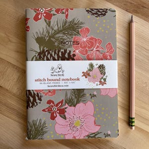 May include: A floral-patterned notebook with a pencil. The notebook has a gray background with pink and red flowers, pinecones, and green pine needles. The text "NOTES" is at the top. The notebook is 8.5" x 5.5" and has 56 blank pages.