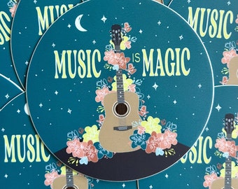 Op de afbeelding: Een ronde sticker in tealblauw met een witte halve maan, sterren en een bloemmotief rond een akoestische gitaar. De tekst "MUSIC IS MAGIC" staat in gele letters.