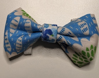 Puede incluir: Una pajarita azul y blanca con un estampado floral verde y blanco. La pajarita está atada con una banda estampada azul y blanca.