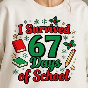May include: White sweatshirt with the text "I Survived 67 Days of School" in red, green, and black. The design includes illustrations of books, snowflakes, stars, holly, and a pencil.