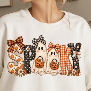 May include: A white long-sleeve sweatshirt featuring the word SPOOKY in large decorative letters. The letters are decorated with orange and black plaid patterns, polka dots, ghost illustrations, small pumpkins, and floral accents.