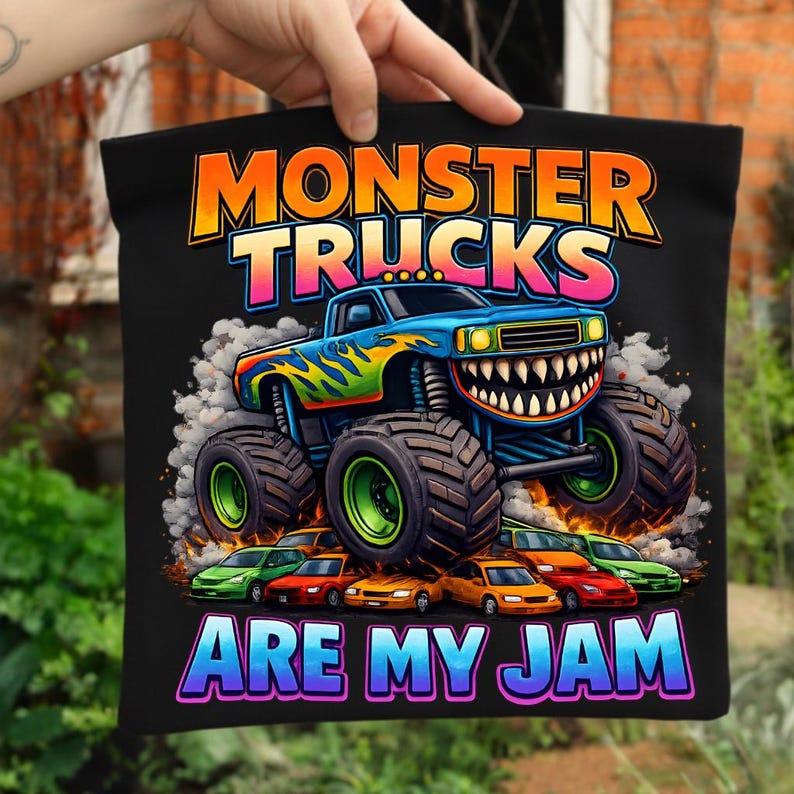 Puede incluir: Bolso tote negro con un gr&aacute;fico colorido de un monster truck con una sonrisa y el texto "MONSTER TRUCKS ARE MY JAM". El monster truck es azul con llamas verdes y amarillas. Peque&ntilde;os coches debajo.