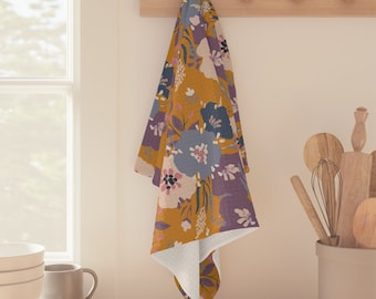 May include: A mustard yellow kitchen towel with a floral pattern featuring purple, blue, and pink flowers. The towel is hanging on a wooden rack.
