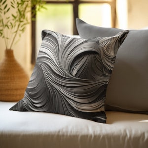 May include: A black and white patterned throw pillow with a swirling design. The pillow is sitting on a white couch with a gray pillow behind it.