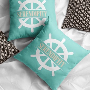 May include: Two turquoise blue throw pillows with white ship wheel designs and the word "SERENDIPITY" in a tan font.