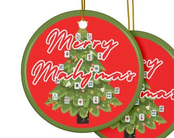 May include: Two round Christmas ornaments with a red background and green trim. The ornaments feature a green Christmas tree decorated with Mahjong tiles. The words "Merry Mahjimas" are written in white script across the front.