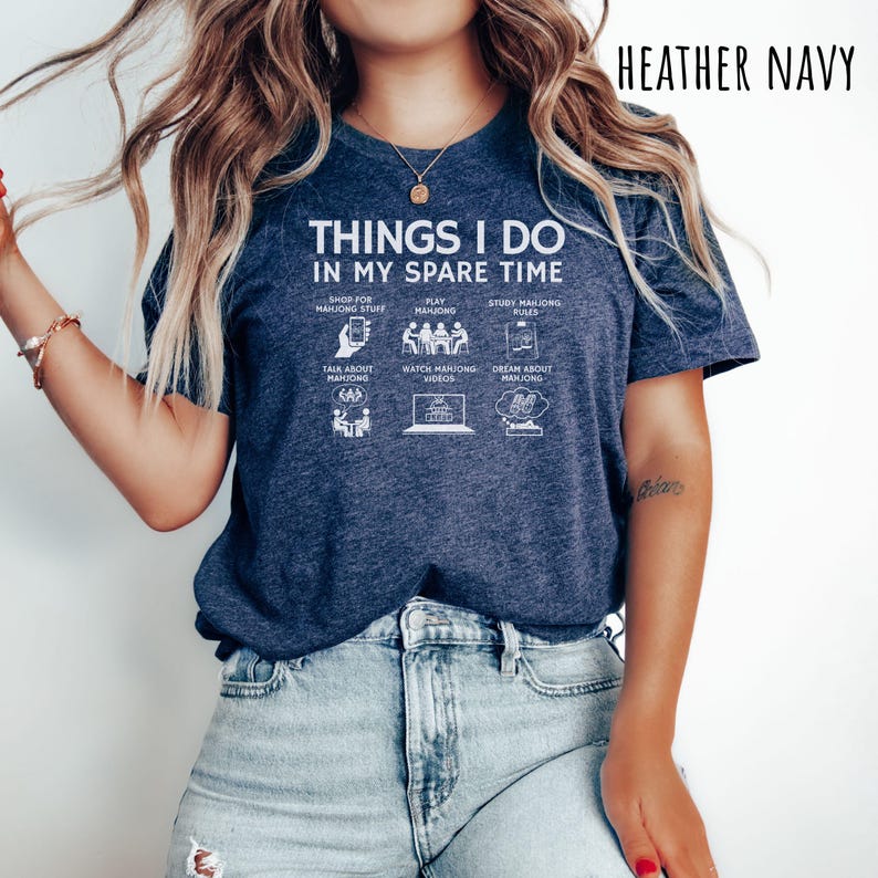 May include: Heather navy blue t-shirt with the text "THINGS I DO IN MY SPARE TIME". The graphic includes icons representing activities like shopping, playing, and studying Mahjong. The shirt is a casual wear item.