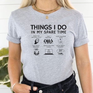 May include: A light gray t-shirt with the text "THINGS I DO IN MY SPARE TIME" and illustrations of activities related to Mahjong. The activities include shopping, playing, studying rules, talking, watching videos, and dreaming about Mahjong.