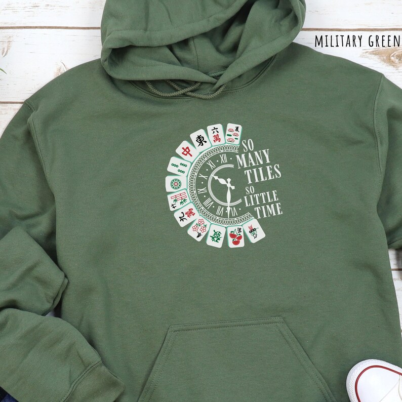May include: Military green hoodie with a front graphic featuring a circular design of Mahjong tiles and the text "SO MANY TILES SO LITTLE TIME". The hoodie has a drawstring hood and a front pocket.