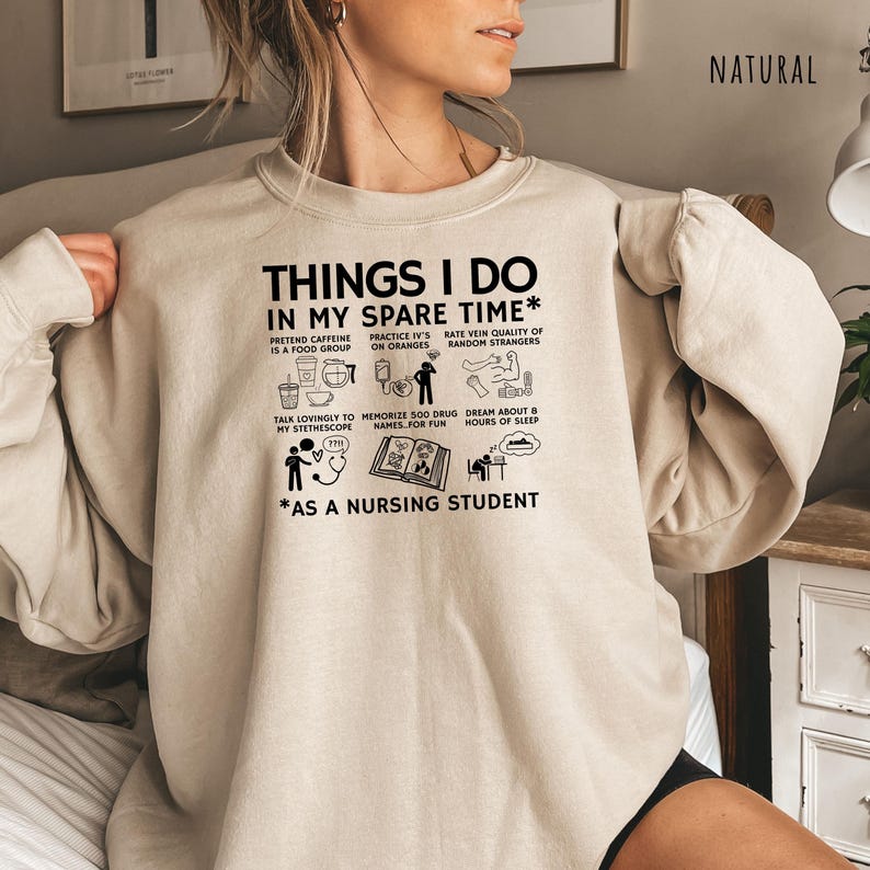 Peut inclure: Un sweat-shirt beige avec l'inscription noire "THINGS I DO IN MY SPARE TIME* AS A NURSING STUDENT". Le motif comprend des illustrations de tasses &agrave; caf&eacute;, de poches IV et d'un st&eacute;thoscope. Le mot "NATURAL" est imprim&eacute; en haut &agrave; droite.