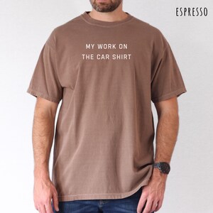 May include: Espresso-colored t-shirt with the text "MY WORK ON THE CAR SHIRT" in white. The shirt is a short-sleeved, crew neck style. The model is wearing a black watch. The shirt is a solid color.