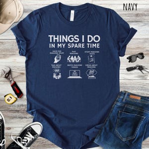 May include: Navy blue t-shirt with the text "THINGS I DO IN MY SPARE TIME" and illustrations of activities like shopping for Mahjong stuff, playing Mahjong, and studying Mahjong rules. The shirt is made of a soft material.