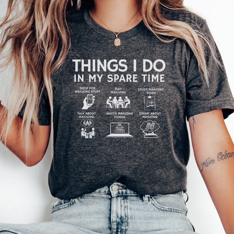 May include: Dark gray t-shirt with white text and illustrations. The shirt reads "THINGS I DO IN MY SPARE TIME" with images depicting activities like playing mahjong, studying rules, and watching videos. A fun, casual tee.