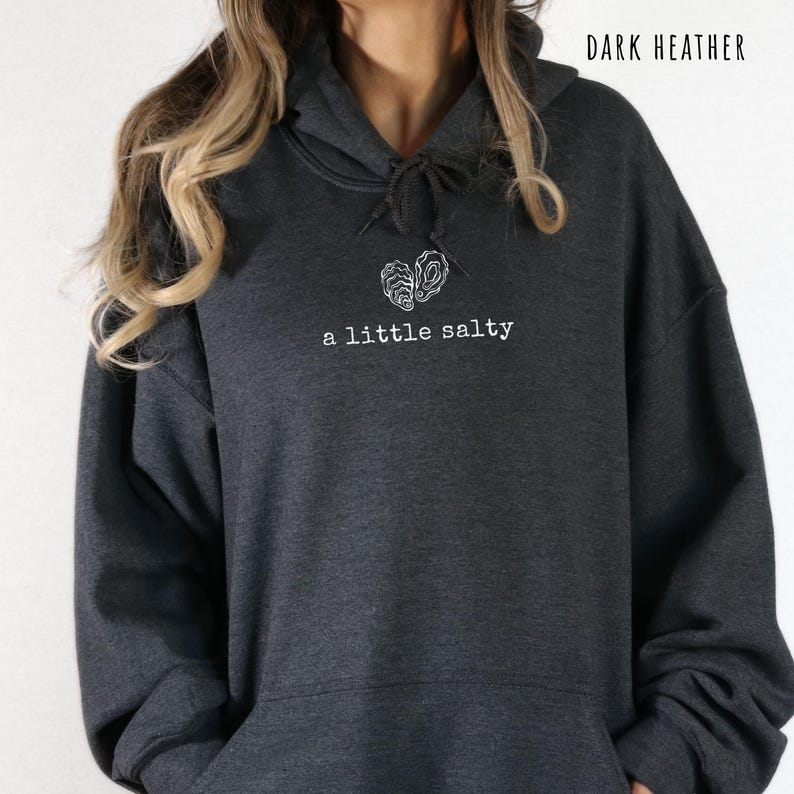 Pode incluir: Moletom cinza escuro mesclado com capuz com cord&atilde;o e bolso frontal. O moletom apresenta um gr&aacute;fico branco de um c&eacute;rebro e o texto "a little salty". As palavras "Dark Heather" s&atilde;o impressas na parte superior.