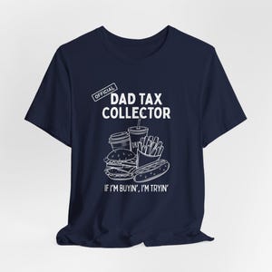 Może przedstawiać: Granatowa koszulka z napisem "DAD TAX COLLECTOR" i grafiką fast food. Koszulka zawiera r&oacute;wnież frazę "IF I'M BUYIN', I'M TRYIN'" w białym tekście.