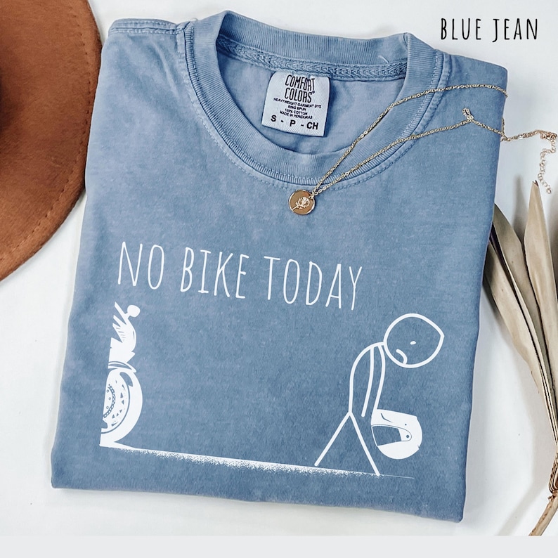 May include: Blue jean Comfort Colors t-shirt with the text "NO BIKE TODAY" and a graphic of a motorcycle and a dejected stick figure. A gold necklace with a pendant is draped across the shirt.