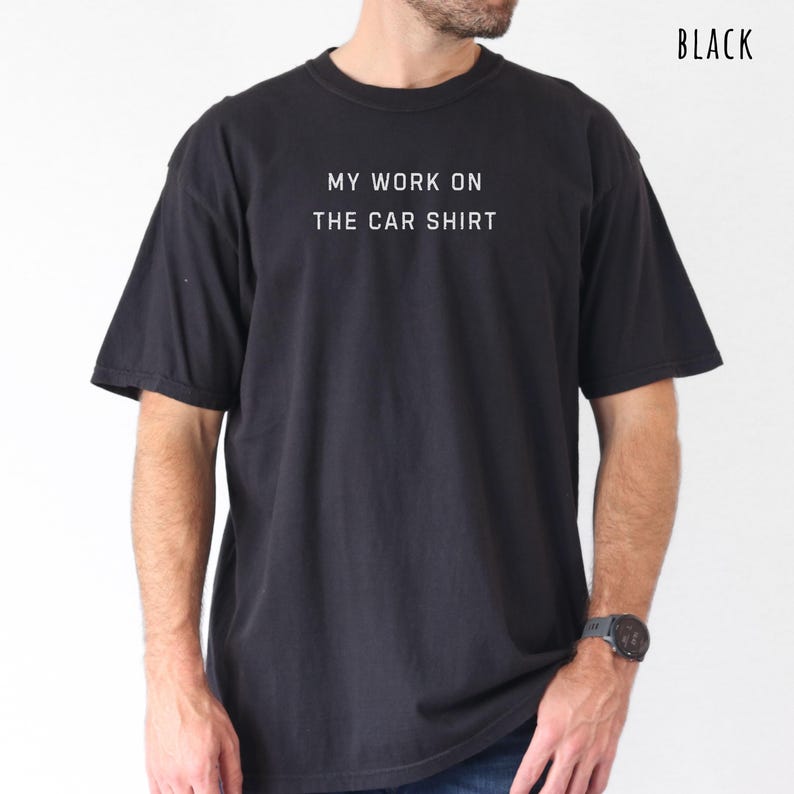 May include: Black t-shirt with the text "MY WORK ON THE CAR SHIRT" in white. The shirt is a crew neck style and has short sleeves. The word "BLACK" is printed in the upper right corner.