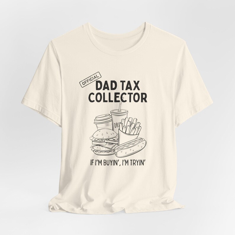 Może przedstawiać: Kremowa koszulka z napisem "OFFICIAL DAD TAX COLLECTOR" i grafiką fast food. Poniżej grafiki znajduje się fraza "IF I'M BUYIN', I'M TRYIN'".