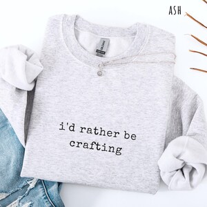 Pu&ograve; includere: Felpa grigio chiaro con la scritta nera "i'd rather be crafting". La felpa ha maniche lunghe e girocollo. Una collana d'argento con un piccolo ciondolo &egrave; drappeggiata sul davanti. La parola "ASH" &egrave; visibile.