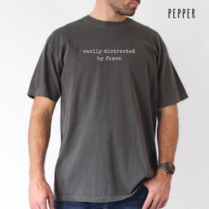 Pu&ograve; includere: T-shirt grigio scuro con la scritta bianca "easily distracted by foxes". La maglietta ha maniche corte e una vestibilit&agrave; rilassata. La parola "PEPPER" &egrave; stampata in alto a destra. La maglietta &egrave; color pepe.