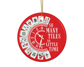 May include: A circular, red ceramic ornament with a gold hanging string. It features a clock design with Mahjong tiles and the text "SO MANY TILES SO LITTLE TIME".