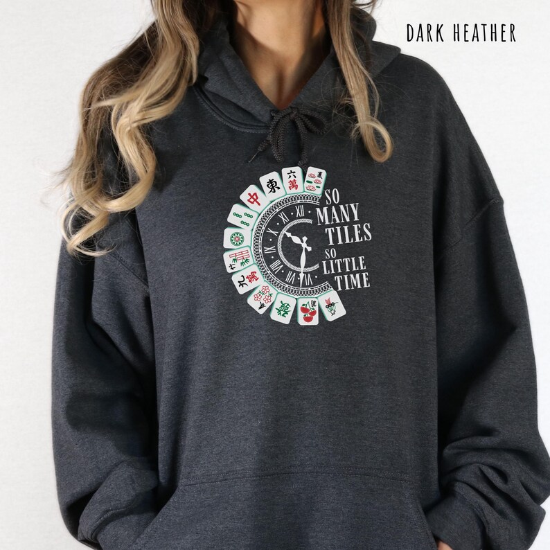 May include: Dark heather gray hoodie with a circular graphic featuring Mahjong tiles and the text "SO MANY TILES SO LITTLE TIME." The design includes a clock face and Chinese characters. The hoodie has a drawstring hood.