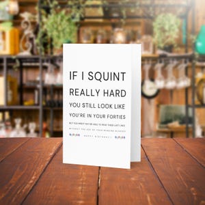 May include: A white birthday card with black text that reads "If I squint really hard you still look like you're in your forties. But you might not be able to read these last lines without the use of your reading glasses. Happy Birthday!"
