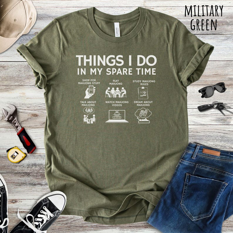 May include: Military green t-shirt with the text "THINGS I DO IN MY SPARE TIME" and illustrations of Mahjong-related activities. The shirt includes the text "SHOP FOR MAHJONG STUFF", "PLAY MAHJONG", "STUDY MAHJONG RULES", "TALK ABOUT MAHJONG", "WATCH MAHJONG VIDEOS", and "DREAM ABOUT MAHJONG".