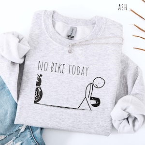May include: Light gray sweatshirt with the text "NO BIKE TODAY" and a stick figure design. The design includes a motorcycle and a dejected person holding a helmet. The sweatshirt has long sleeves and a crew neck.