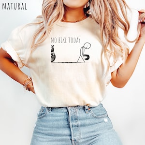 May include: Cream-colored t-shirt with the text "NO BIKE TODAY" above a stick figure and motorcycle graphic. The stick figure appears dejected, holding a helmet. The word "NATURAL" is printed in the upper left corner.