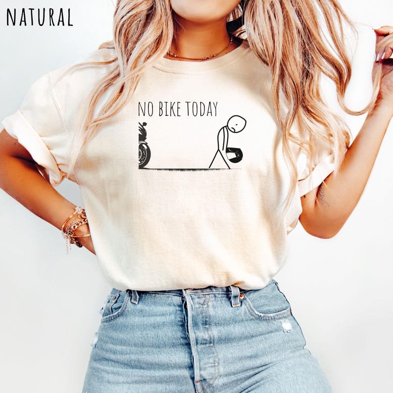 May include: Cream-colored t-shirt with the text "NO BIKE TODAY" above a stick figure and motorcycle graphic. The stick figure appears dejected, holding a helmet. The word "NATURAL" is printed in the upper left corner.