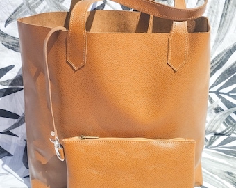 May include: A brown leather tote bag with a matching brown leather pouch. The tote bag has two top handles and a detachable shoulder strap. The pouch has a zipper closure.