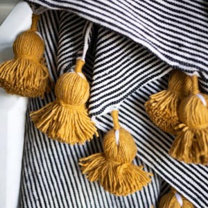 May include: Black and white striped throw blanket with yellow pom-poms on the edges.