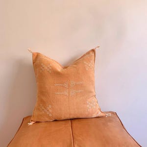 May include: A light orange throw pillow with a white geometric pattern. The pillow is made of a soft, textured fabric and has a subtle sheen.