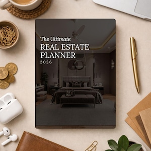 Puede incluir: Un planificador titulado "The Ultimate Real Estate Planner 2026" con una cubierta oscura que presenta un diseño interior de dormitorio. Un bolígrafo dorado, una taza de café, monedas y otros útiles de oficina rodean el planificador.