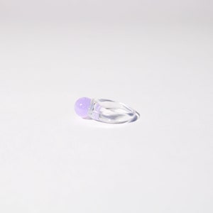 Peut inclure: Une bague transparente avec une pierre ronde de couleur violette claire et scintillante.