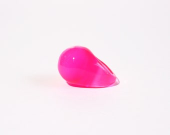 May include: A bright pink resin ring. The ring is shaped like a teardrop and has a glossy finish.