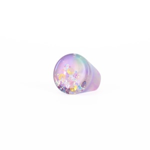 May include: A purple and pink resin ring with iridescent glitter embedded inside. The ring is oval shaped and has a smooth, glossy finish.