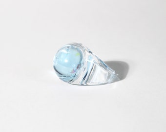 May include: A clear glass ring with a light blue orb in the centre. The orb has a few small, colourful flecks inside.
