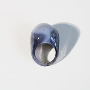 Peut inclure: Une bague en agate grise et blanche avec une surface lisse et arrondie. La bague est faite de pierre naturelle et présente un motif unique et tourbillonnant.