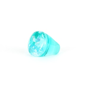 Peut inclure: Une bague bleu turquoise avec un dessus en résine transparente rempli de paillettes irisées.