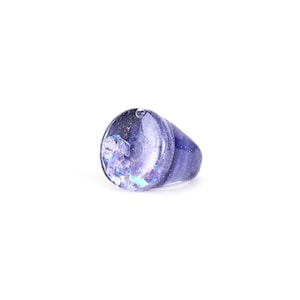 Peut inclure: Une bague en résine violette avec des paillettes irisées incrustées à l'intérieur. La bague a un dessus arrondi de forme ovale.