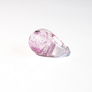 Peut inclure: Une bague en plastique transparente avec des paillettes roses à l'intérieur. La bague est de forme ovale arrondie.