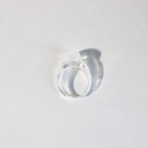 Peut inclure: Une bague en verre transparent avec une grosse pierre ronde en verre transparent.