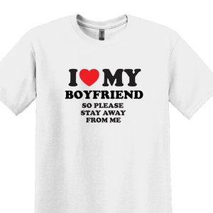May include: White t-shirt with black text that reads "I love my boyfriend so please stay away from me". A red heart is in the text.