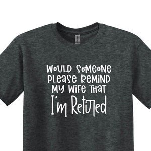 May include: Dark heather grey t-shirt with the text "Would someone please remind my wife that I'm retired".