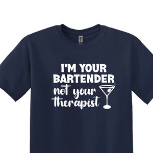 Pode incluir: Camiseta azul marinho com texto branco "I'M YOUR BARTENDER not your therapist" e um gráfico de copo de Martini. A camiseta tem gola redonda e mangas curtas.